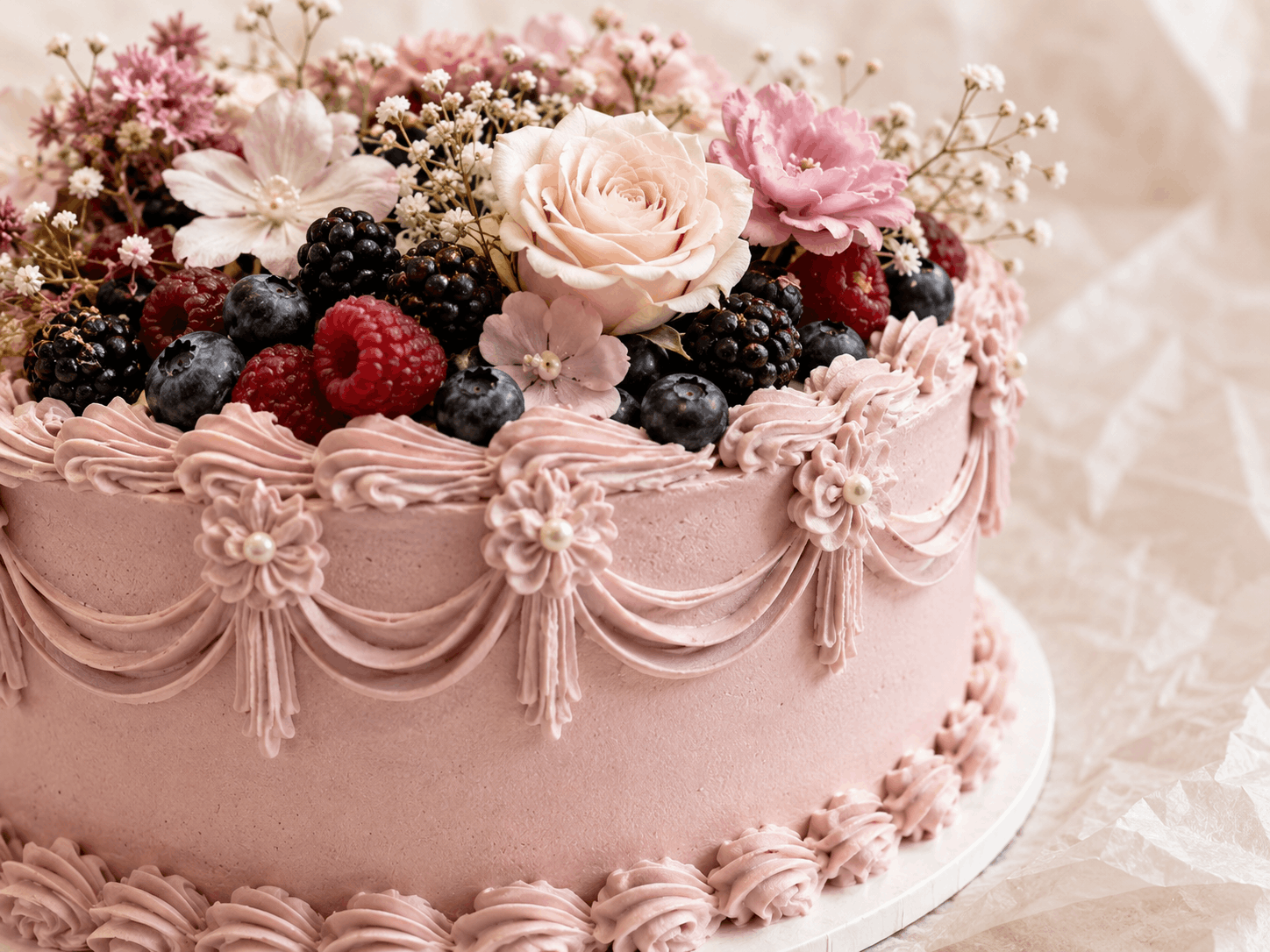 Nahaufnahme einer pastellrosa Torte mit Creme, Blüten und Beeren